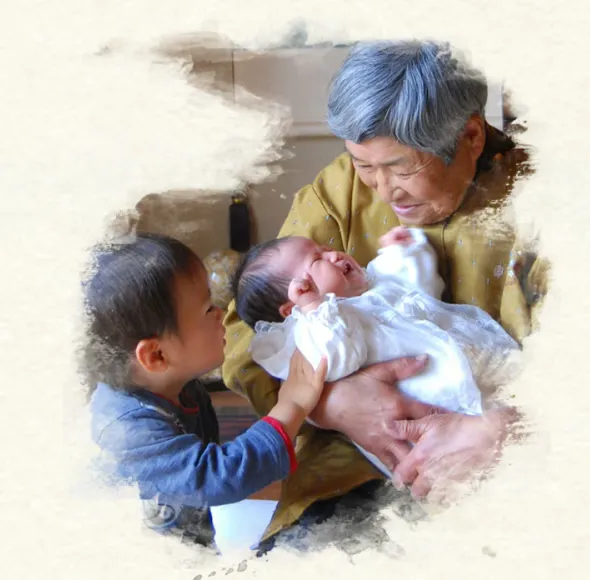 祖母に抱かれた赤ちゃんの手を握る幼い孫