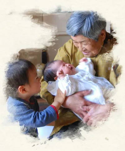 祖母に抱かれた赤ちゃんの手を握る幼い孫