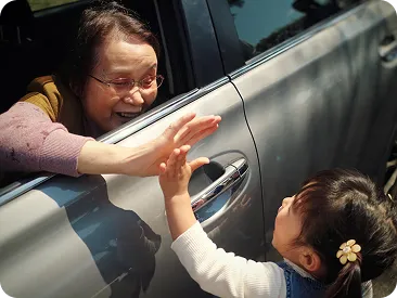 車の窓越しに孫と手を合わせる祖母
