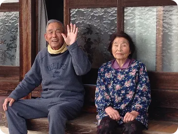 縁側に並んで座り手を振るご夫婦